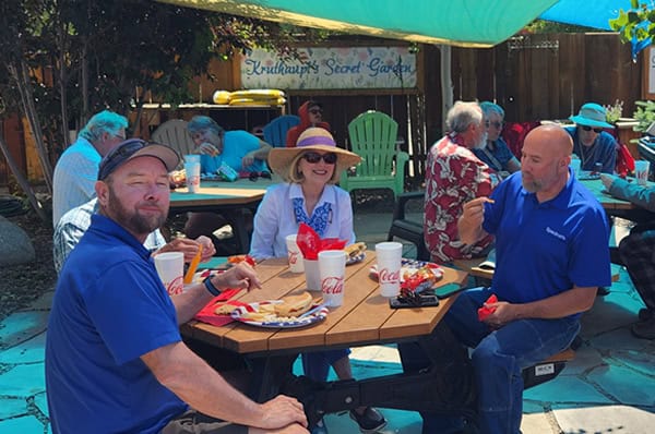 A event at Six Points Patio with groups of people eating and smiling from picnic tables under triangular sunshades.