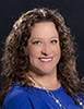 Alicia Corliss smiles in this photo wearing a royal blue shirt and silver necklace.