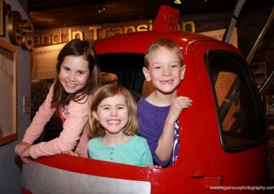 Three kids at the CB Museum Hands on History display grin from an antique red ski Gondola.