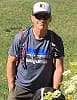 Doug Tredway hiking in a field wearing a lightweight backpack, sunglasses, and t-shirt.