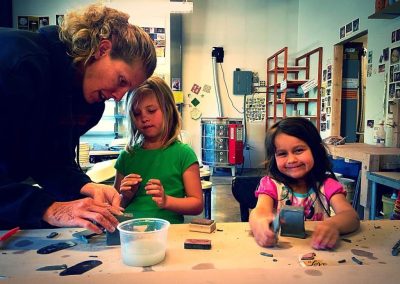 Two young Gunnison Arts Center Mud Puppies use rubber stamps with an instructor.