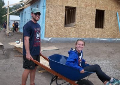 Habitat for Humanity Bike and Build Crew Members: one in a wheel barrow and the other pushing her.