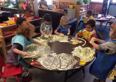 Six preschoolers finger painting with yellow shaving cream on a table.