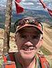 Mike Keig at the top of a mountain with red prayer flags waving in the wind.