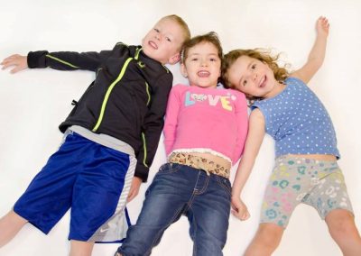 Three Paradise Place Kiddos smile as they pose for the camera against a white background.