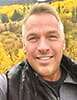 Steve Bolton takes a selfie in front of golden aspen trees on a mountain.