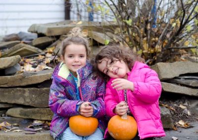 Two Preschool Gals holding pumpkins and wearing bright winter coats at Paradise Place.