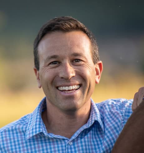 Jason Berv, PH.D. smiling outside wearing a blue plaid shirt.