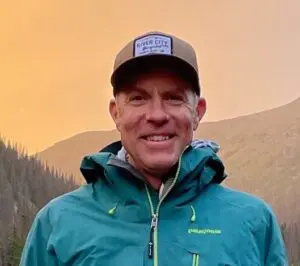 Jake Jones wearing a teal jacket against a mountain sunset.