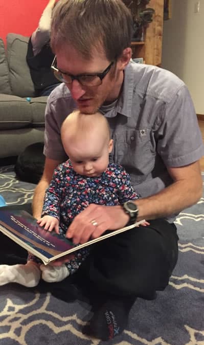 Baby June and her dad, Greg Chase, site on the living room floor reading an Imagination Library story together.