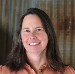 Lyndie Kenlon smiles in front of a wooden wall.