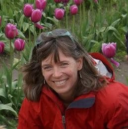 Marilyn Krill smiles wearing a red jacket in a field of magenta tulips.