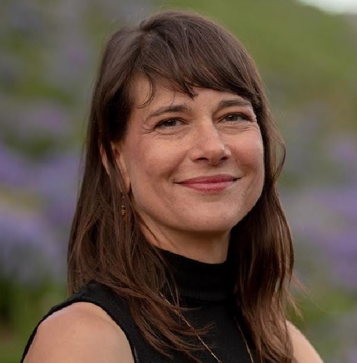 Shelley Popke smiles in a sleeveless black top from a field of purple flowers and greenery.