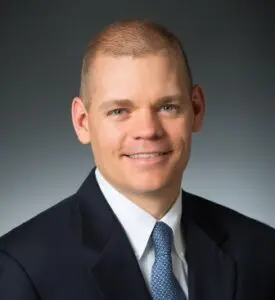 Brian Pugh in a dark navy blue suit and blue tie.