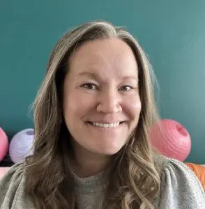 Brieanna Radford with her head turned slightly and smiling in a room with teal walls and pink paper lanterns.