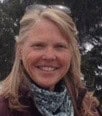 Janice Welborn smiles wearing sunglasses on top of her head and a scarf. 