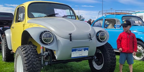 A souped up yellow and gray Volkswagon Beetle and a young child in a red jacket at the Gunnison Car Show.