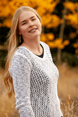 Meredith Diamond smiling in a field of tall grass with orange trees behind her