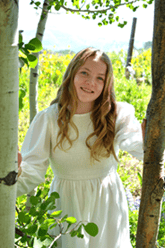 Kailyn Japuntich peeks through two aspens in a white dress.