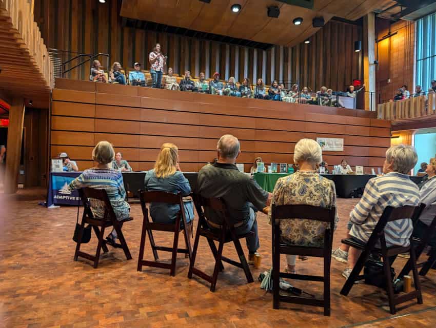 group of people seated on the main floor watching a woman speak from above 