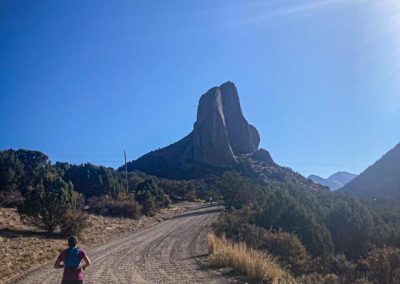 woman running away from camera on dirt road toward rock tower in the background