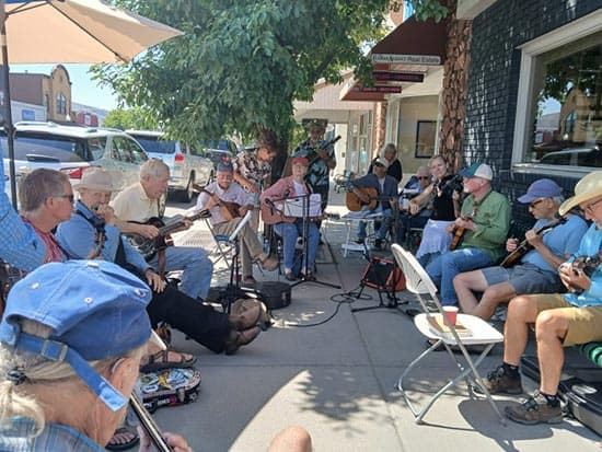 group of musicians sitting on a sidewalk on a sunny Gunnison Day