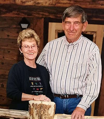 Nancy and Dan Tredway402x458 Nancy and Dan Tredway standing in front of a log building by a log fence.