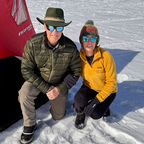 lisa-rodman-1 man wearing olive green cowboy hat and jacket and woman wearing winter hat and bright yellow jacket smiling on kneeling on ice-covered Blue Mesa