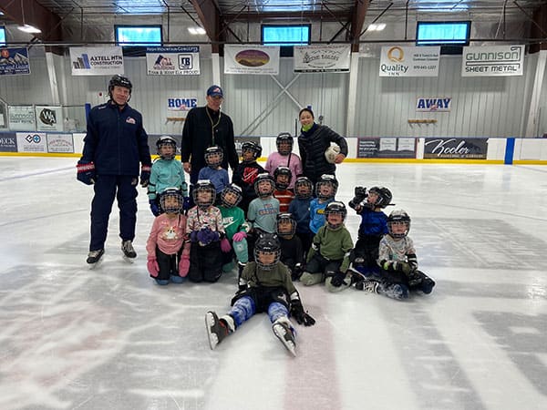 WEHA three adults and a group of children all in hockey gear posing on at ice rink