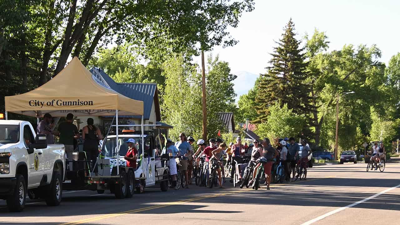 group of bikers following the City of Gunnison trailer with two musicians performing on it