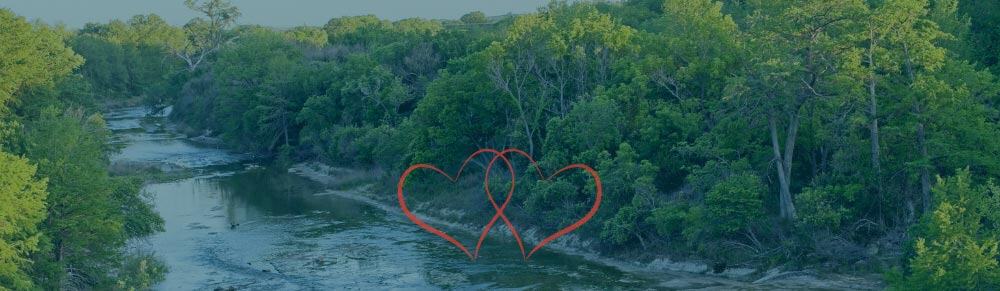 Support-for-Texas-blog-post-hero Photo of Guadlupe River in Kerrville, TX with two interlocking red hearts over it.