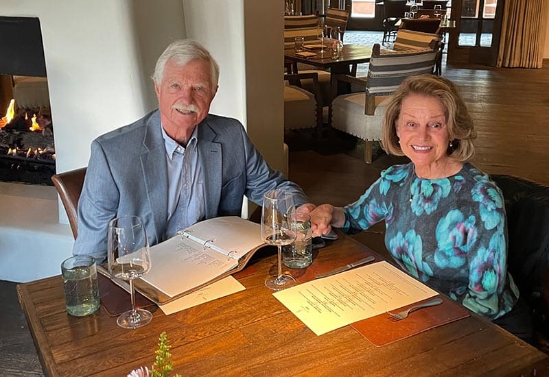 gary-and-bettye smiling man and woman sitting in a restaurant holding hands