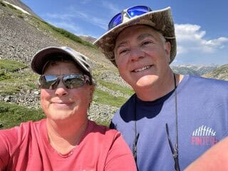 two people hiking a trail through a meadow of wildflowers on a sunny summer day